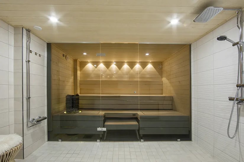 Saunan lasiseinä. Sauna LED-valaistuksella ja lauteisiin integroidulla pilarikiukaalla.