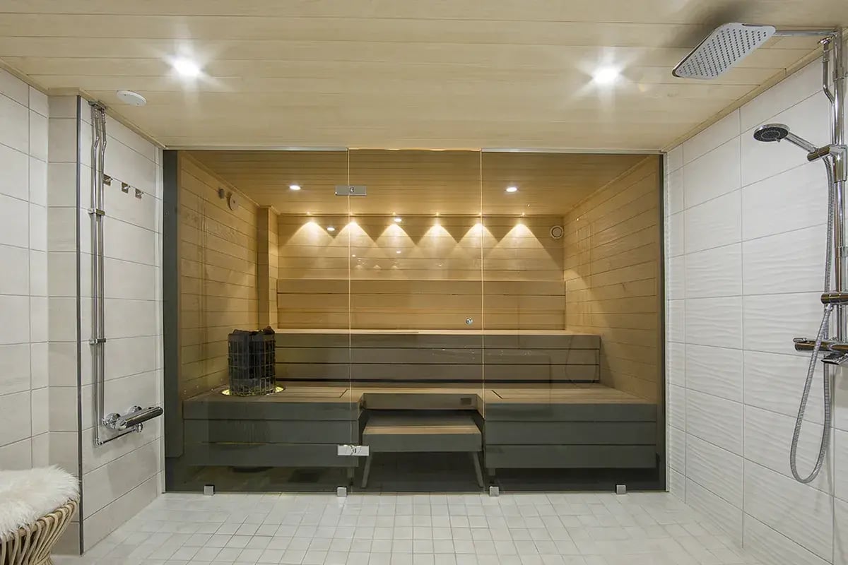 Saunan lasiseinä. Sauna LED-valaistuksella ja lauteisiin integroidulla pilarikiukaalla.