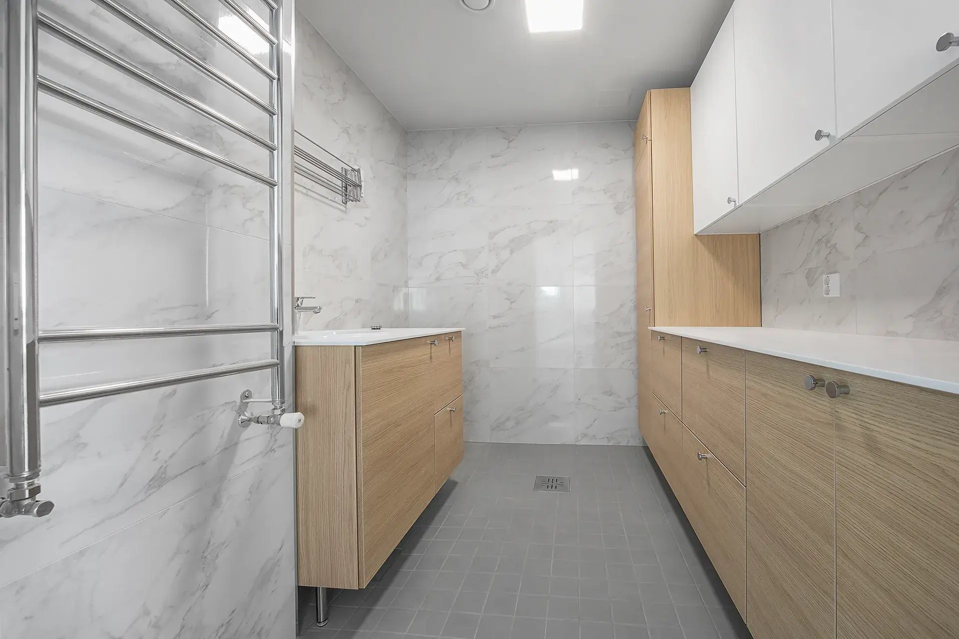 Remontoitu kodinhoitohuone vaaleilla kalusteilla ja marmorikuosisella seinälaatalla